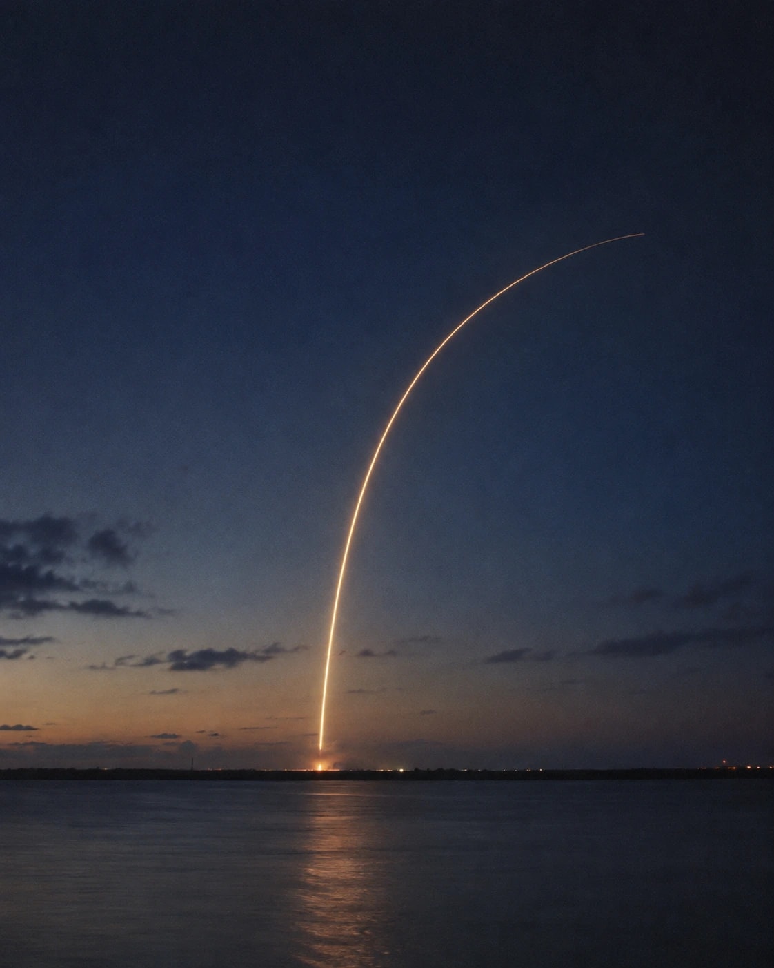 Long-exposure light trail of a distant rocket launch across the water at dusk